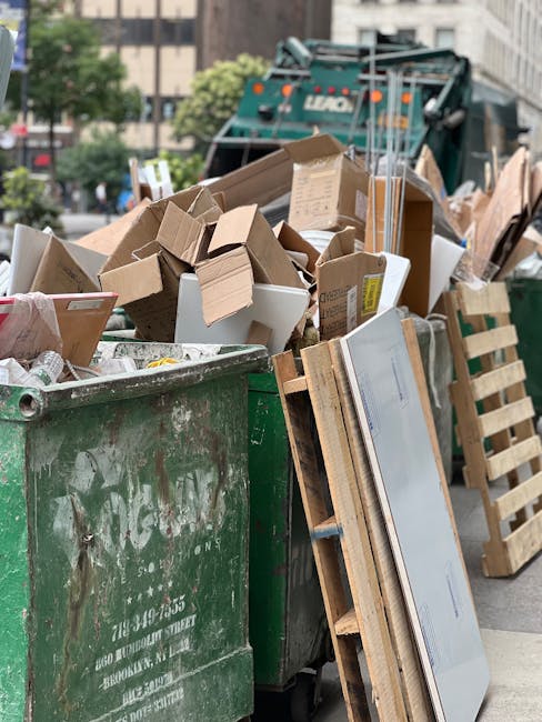 A street scene featuring a white commercial rubbish collection truck parked alongside a row of old, multi-story buildings with weathered facades and sash windows. The truck's rear compactor is open, r